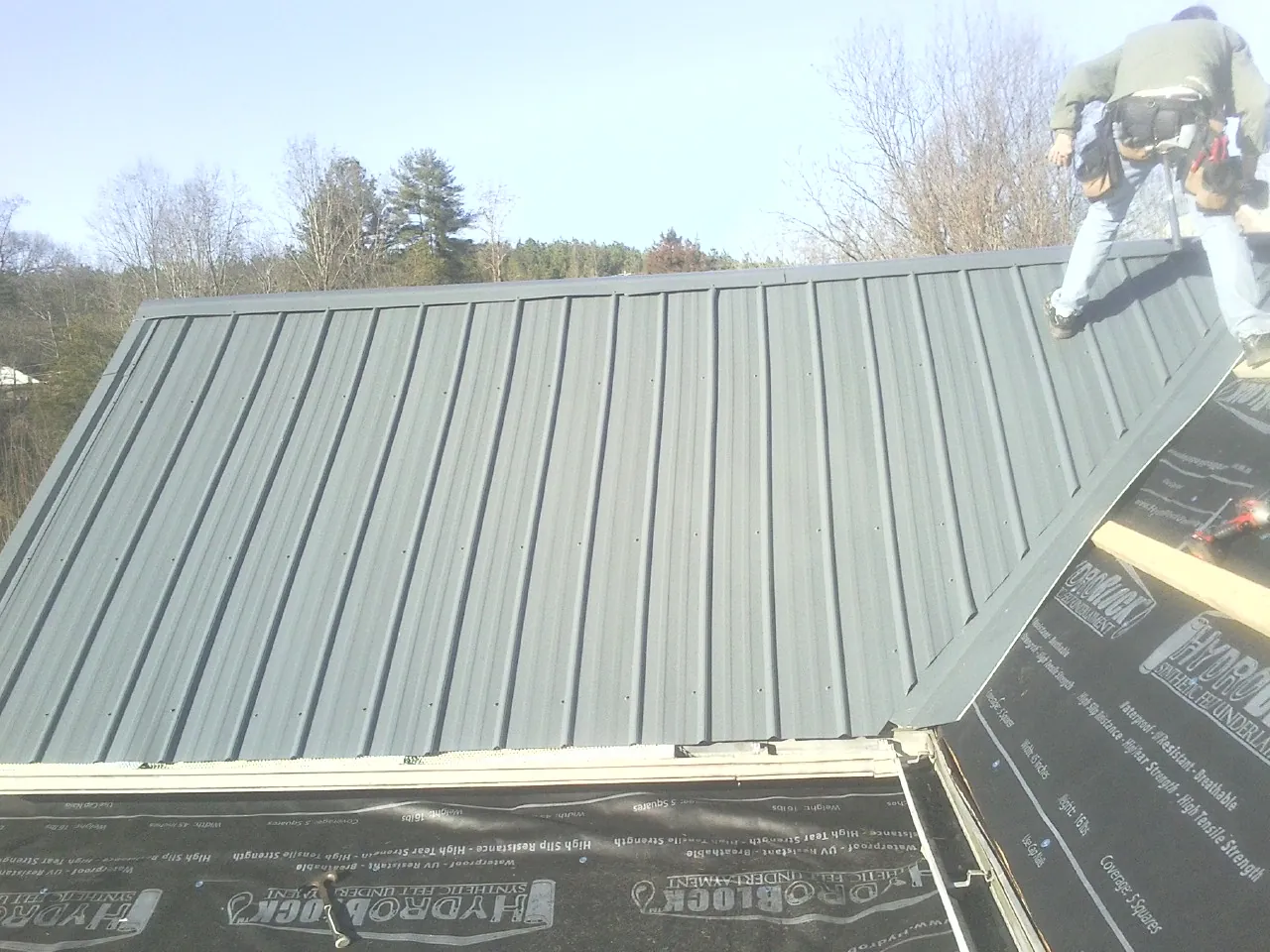 Crew installing dark green standing seam panels over synthetic underlayment in Etlan
