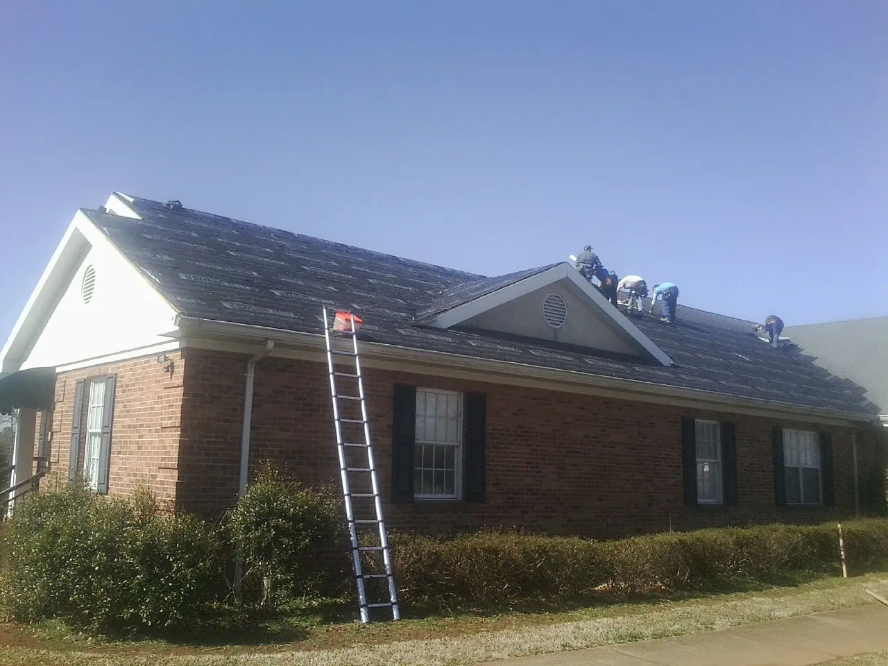 Crew tearing shingles off a brick ranch roof with a ladder set — Metal Roof Repair work by our crew in Etlan