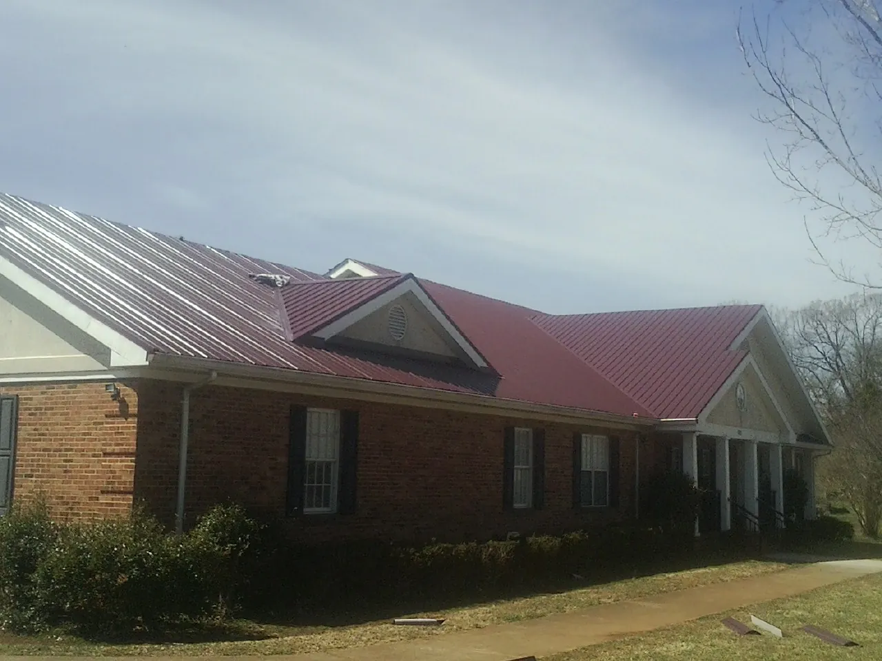 Red metal roof with gabled entries on a long brick building, from a Hail Damage Roof Repair job in Etlan