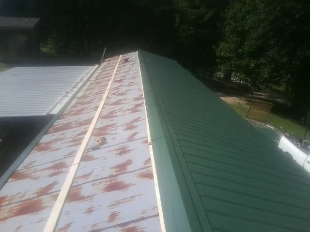 Old rusted panels beside newly installed green metal roofing — Wind Damage Roof Repair by Roofing Brothers in Etlan