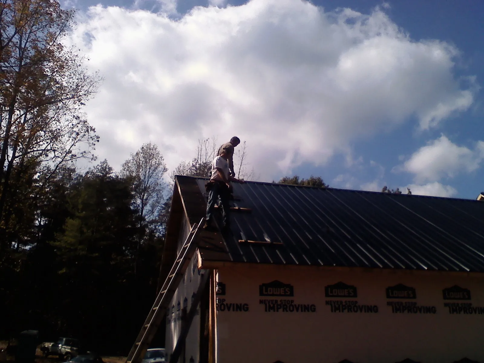 Roofer fastening dark metal panels high against a cloudy sky, from a Roof Inspection job in Etlan
