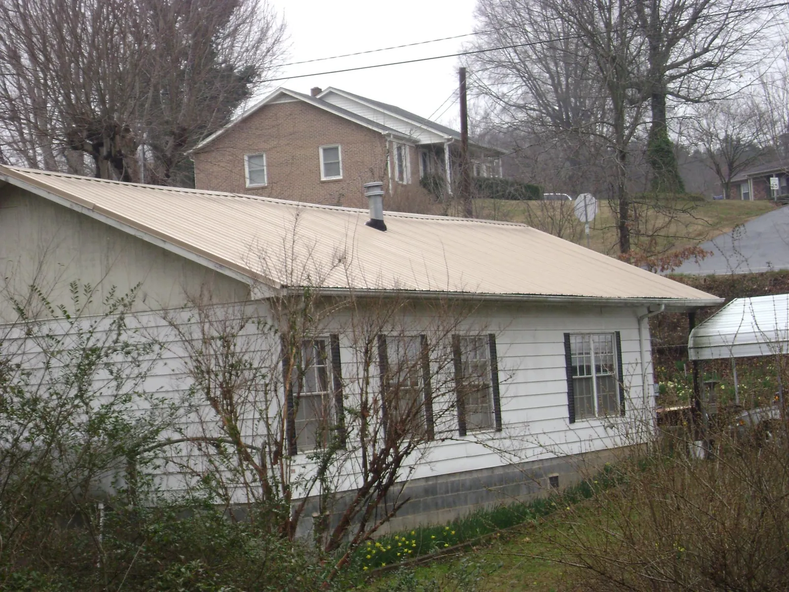 Tan metal roof on a white sided house set into a hillside — Commercial Roofing by Roofing Brothers in Etlan
